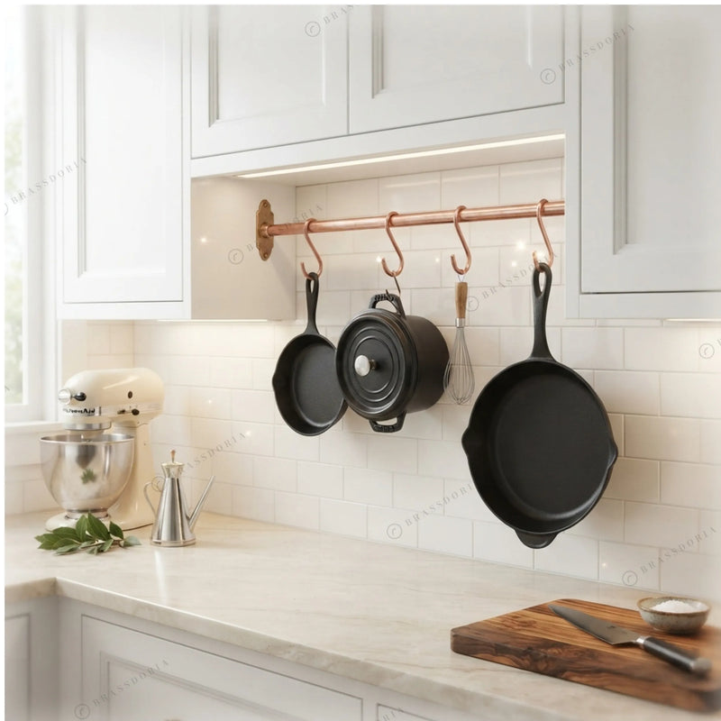 Solid copper pot rail with S-hooks holding cast iron pans in a white kitchen – Brassdoria
