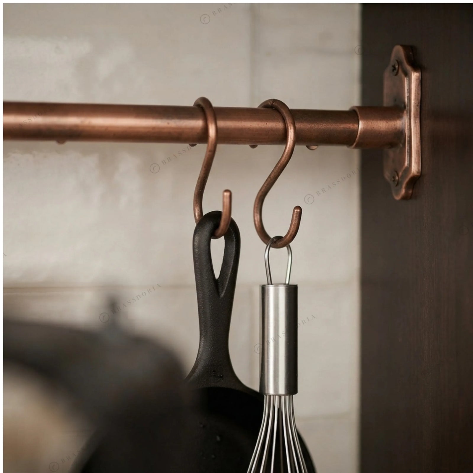 Solid copper pot rail with S-hooks holding cast iron pans in a white kitchen – Brassdoria